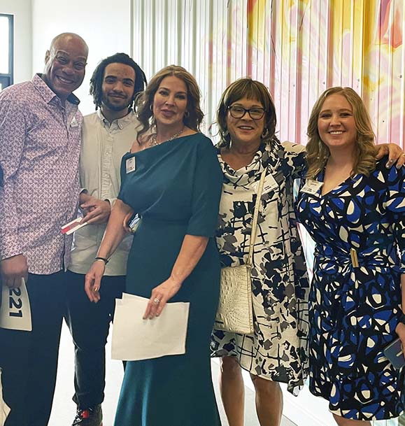 A group of five people, two men and three women, are dressed up and posing at the Power of Work event