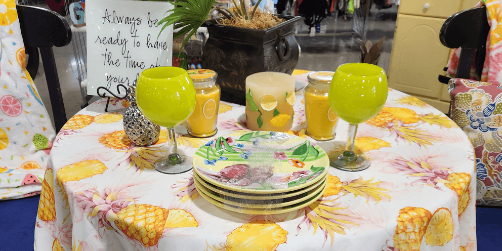 A pineapple tablecloth with tropical leaves plates and glassware on the table.