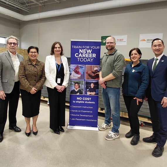 A group of six people stands indoors in front of a GESMN banner promoting career training programs. 