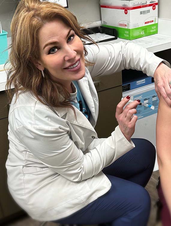 Danielle is shown in a lab coat giving a shot after GESMN training got her a clinic job