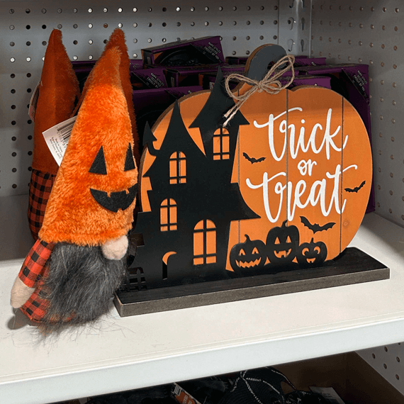 An orange pumpkin gnome next to a pumpkin art decor sign that says "Trick or Treat"