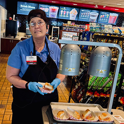 Tammy wears a Kwik Trip uniform and hair net while preparing food for the demonstration area