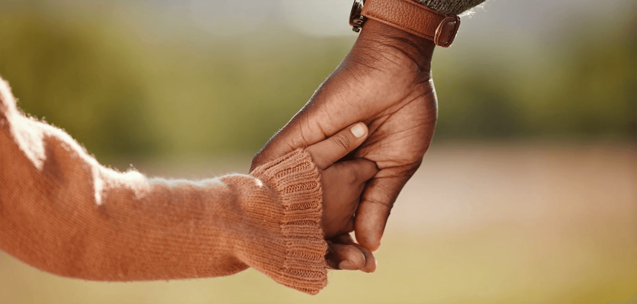 A man's hand clasps a small child's hand