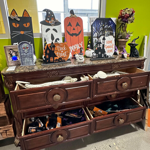 A dresser decorated for Halloween, showcasing items like bats, pumpkins, and eerie ornaments, contributing to a festive look.